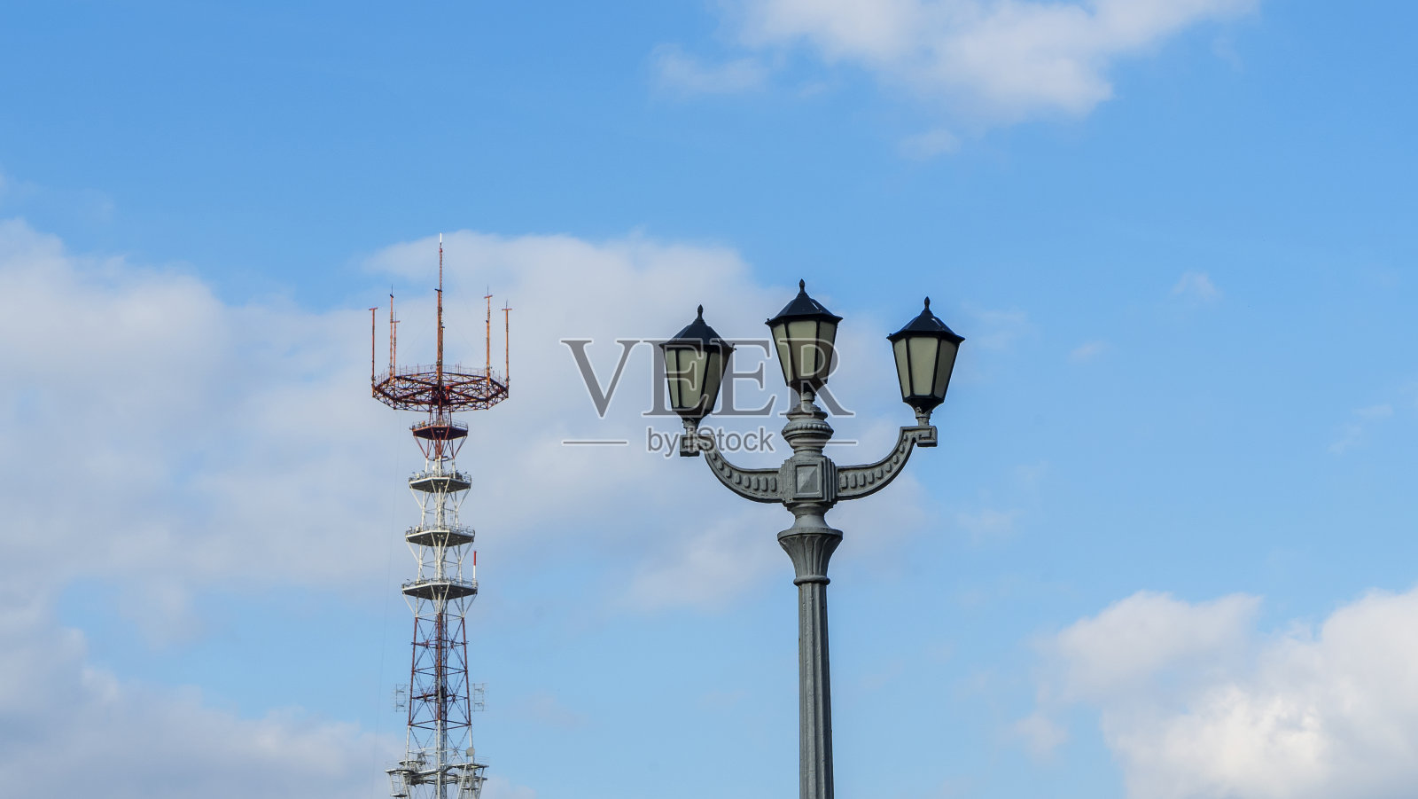 以蓝天白云为背景的电视塔。前景是一盏老式街灯。照片摄影图片
