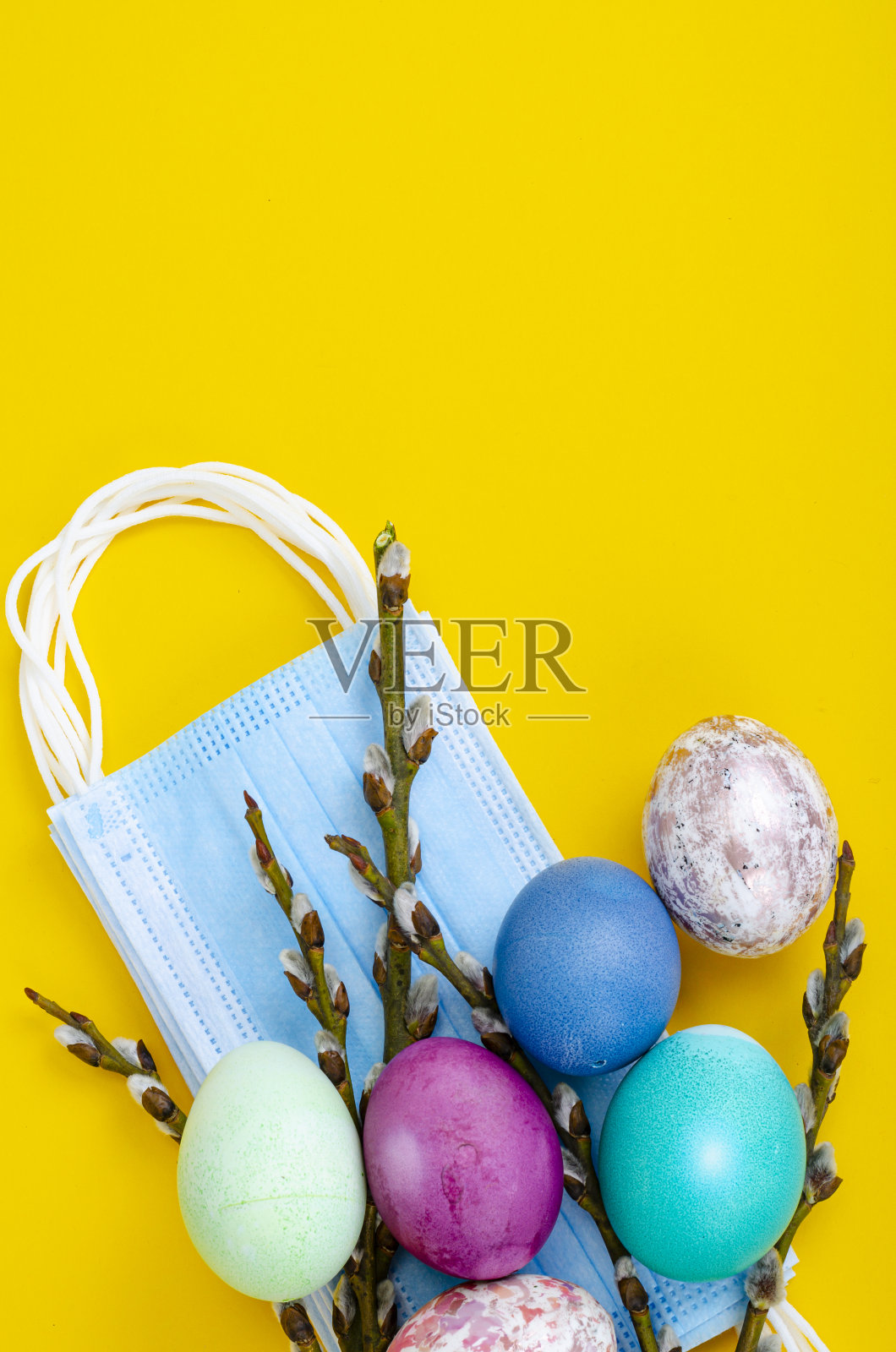 鲜艳的复活节彩蛋，医用口罩，彩色背景上的柳枝。检疫复活节。阻止病毒COVID-19照片摄影图片