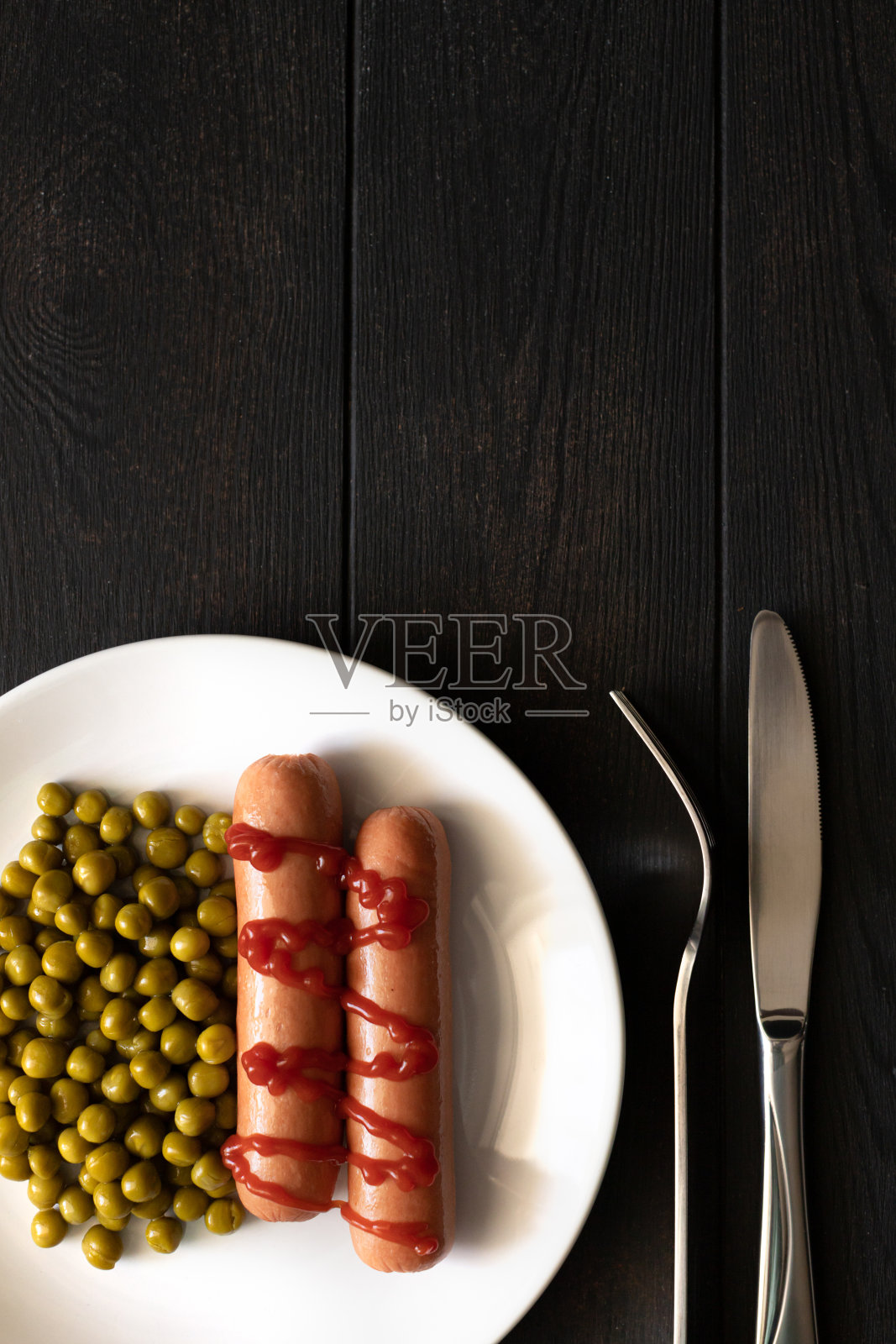 番茄酱香肠，黑底豌豆配菜。照片摄影图片