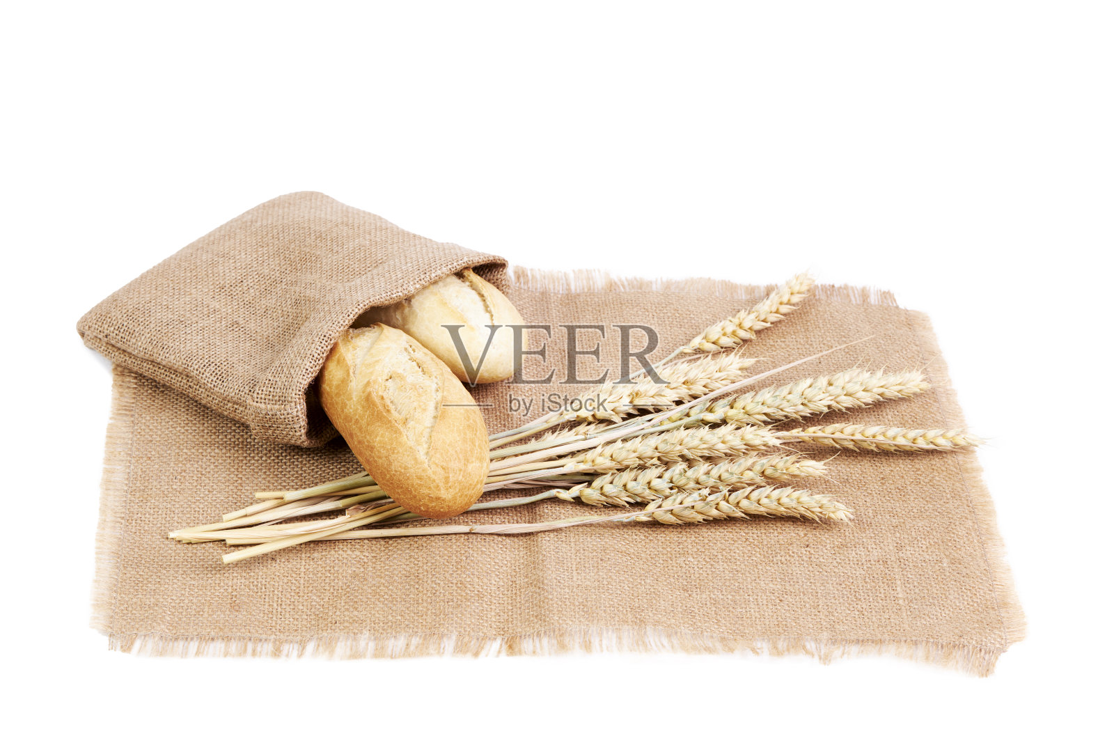 面包长棍装在酒椰酒袋里，旁边是白色背景的酒椰酒布上的麦穗。健康食品的概念照片摄影图片