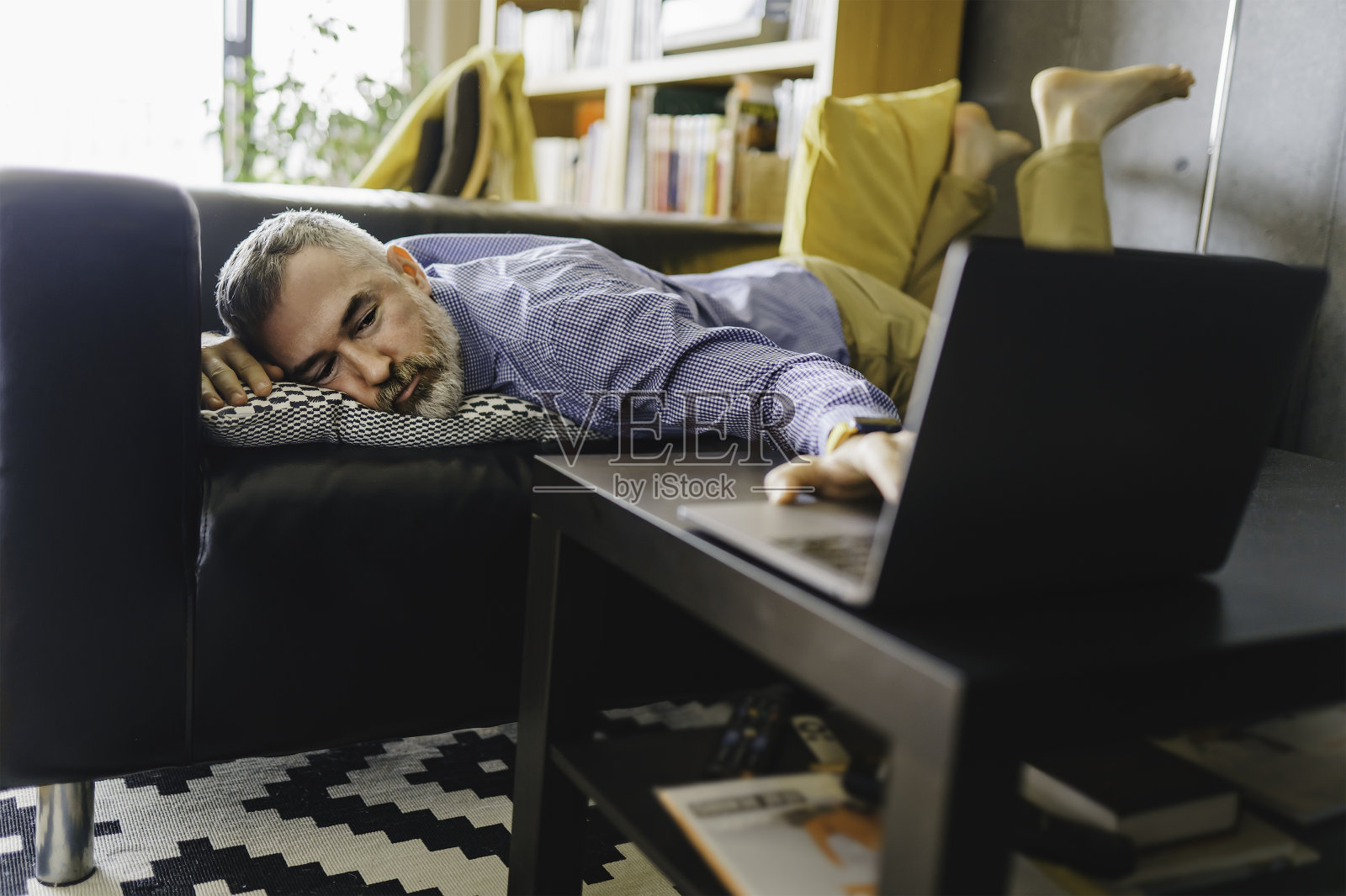 成熟的男人感到压力和厌倦了电脑，躺在沙发上，面前放着笔记本电脑照片摄影图片