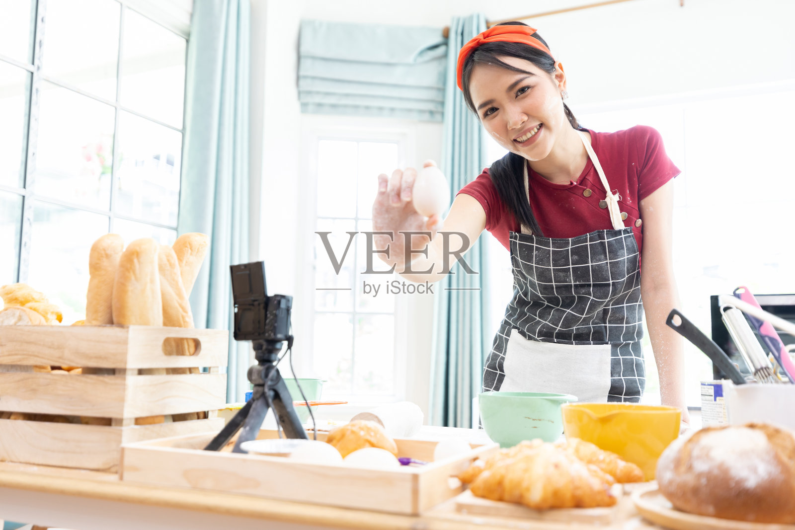 年轻的妇女家庭主妇穿着围裙，拿着新鲜的鸡蛋在厨房里照片摄影图片