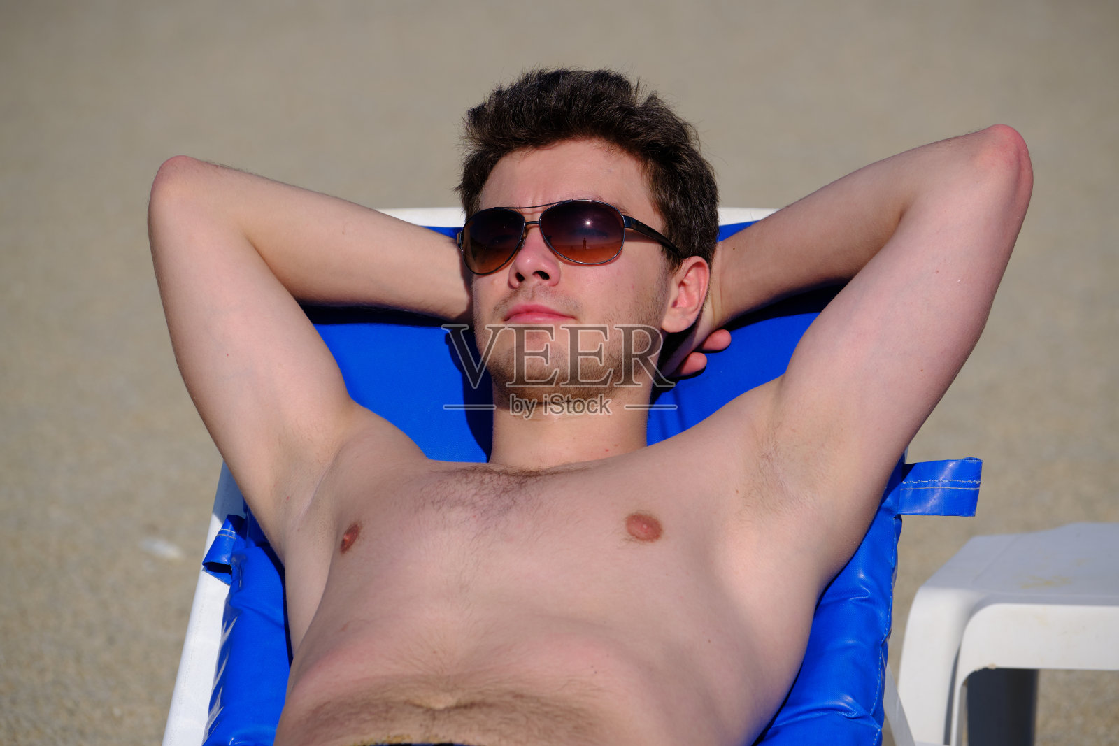 一位25-30岁的年轻英俊男子，黑发，戴着大麻太阳镜，躺在沙滩上的躺椅上，享受日光浴，照片摄影图片