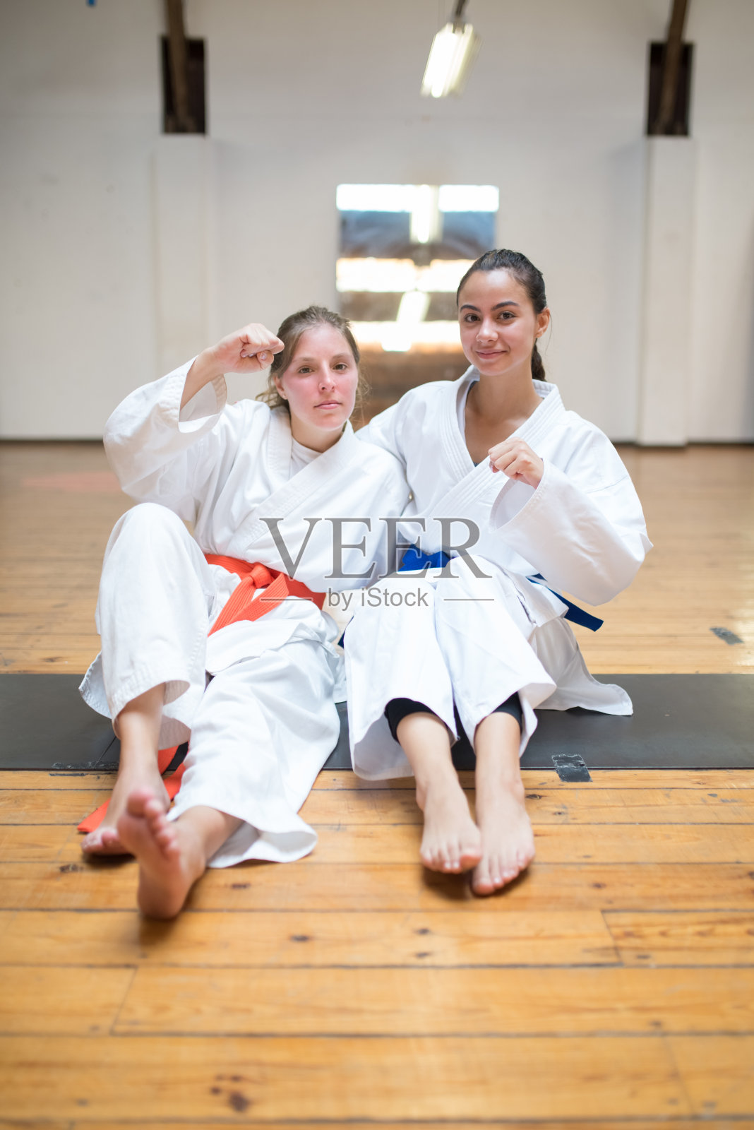 运动的年轻空手道女孩坐在地板上举起拳头照片摄影图片