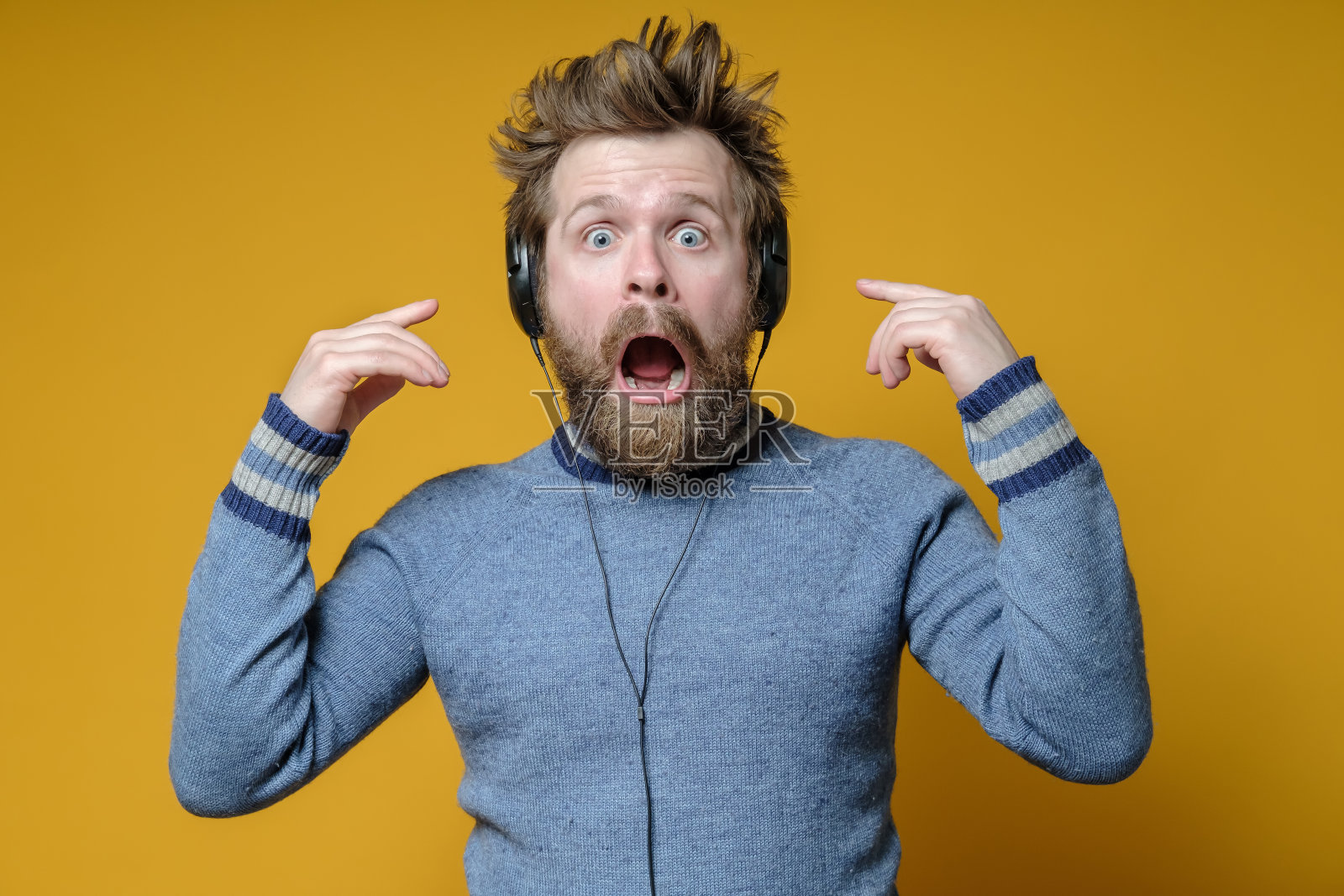 戴着耳机的人欣喜若狂，震惊不已。穿着毛衣的蓬松音乐迷目瞪口呆地盯着镜头。照片摄影图片