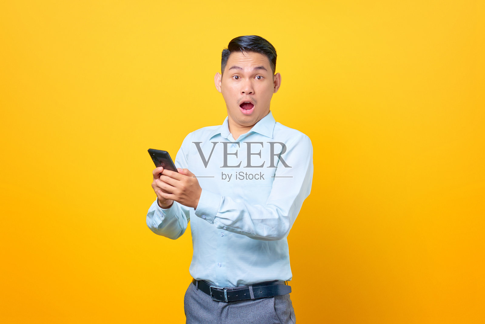 惊讶的年轻英俊的商人拿着智能手机在黄色背景照片摄影图片