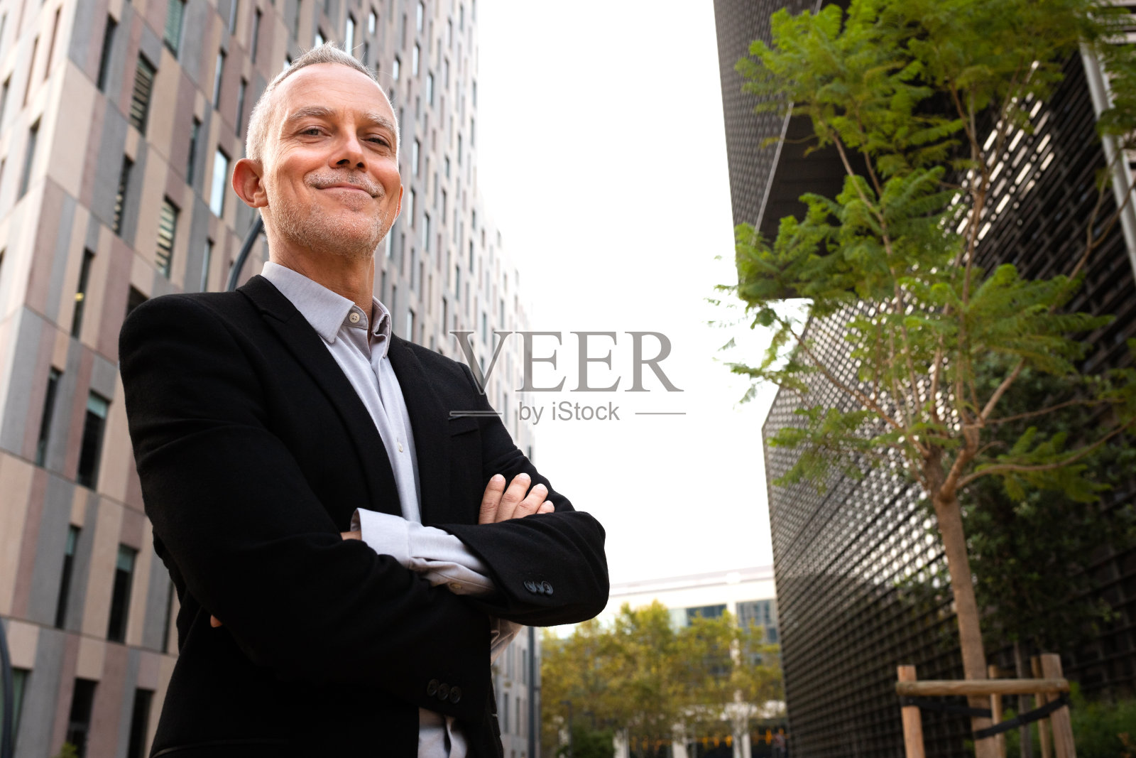 一名白人商人双手交叉站在办公楼旁看着摄像机。本空间照片摄影图片