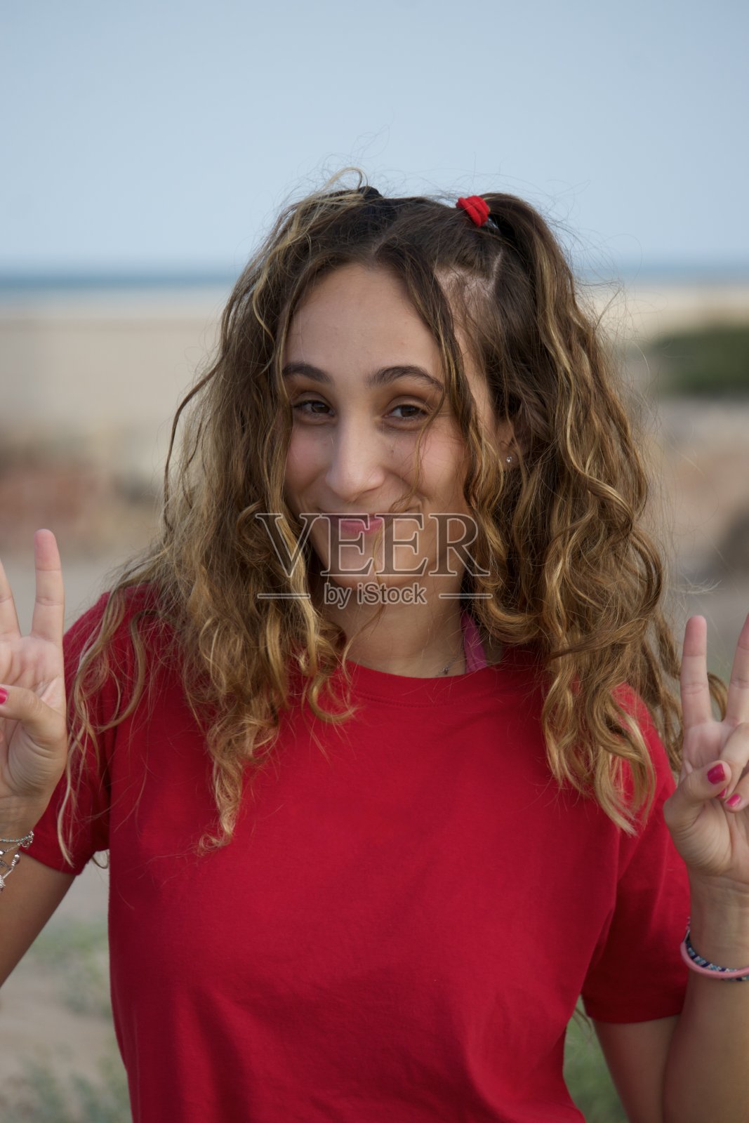 快乐的年轻女子在户外海滩摆姿势，用手指做和平手势。暑假概念。照片摄影图片