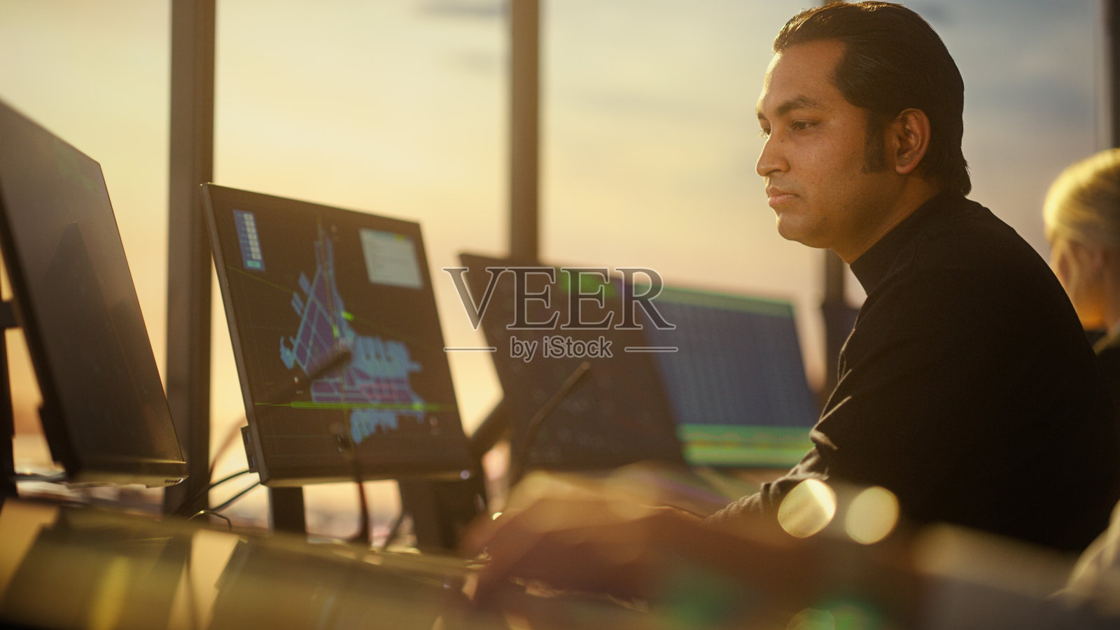 男性空中交通管制员的肖像，戴着耳机在机场塔台通话。办公室里满是桌面电脑显示器，有导航屏幕，飞机飞行雷达数据。照片摄影图片