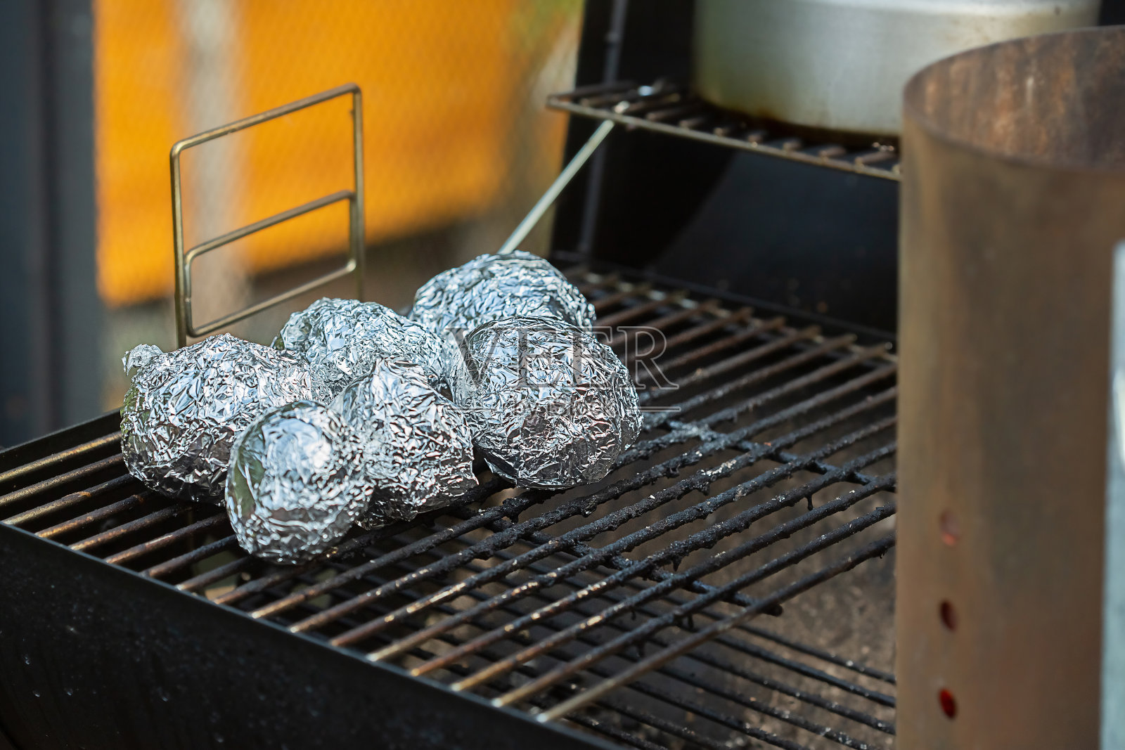 用箔纸包裹的整个土豆在木炭烤架上烤照片摄影图片