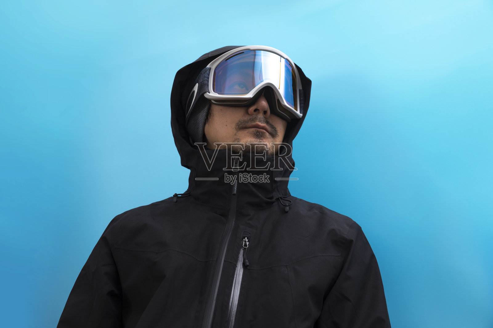 亚洲人在冬季滑雪外套和眼镜上的蓝色背景。照片摄影图片