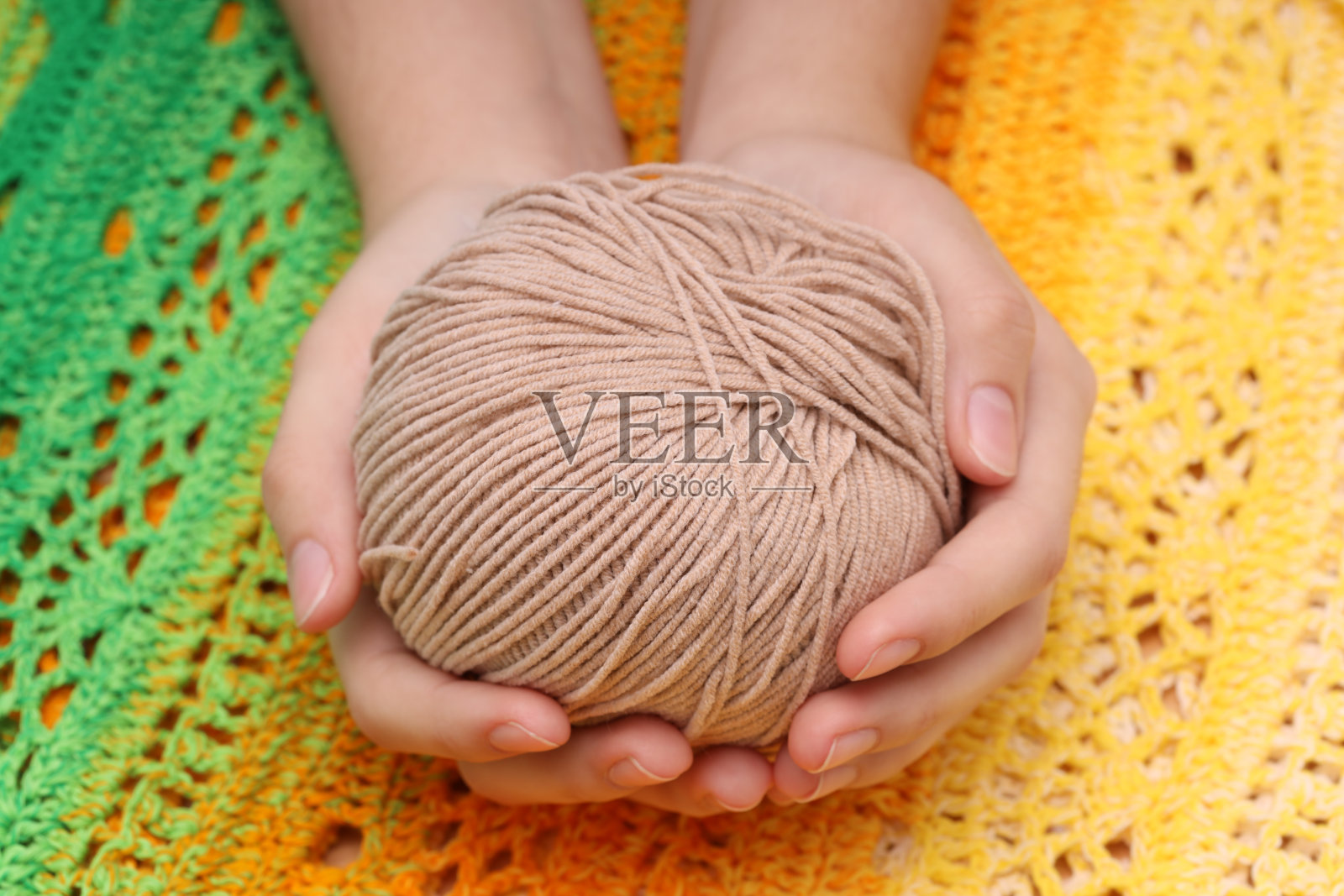 手里拿着一个棕色的毛线球，背景是一块黄绿色的针织台布照片摄影图片