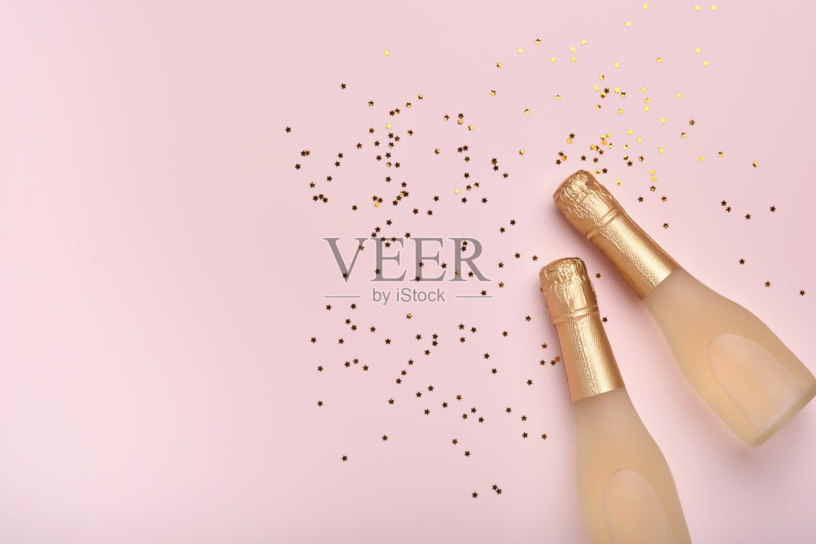 香槟瓶，礼物或礼物盒和金光闪闪的星星五彩纸屑在粉红色的背景。圣诞或新年作文或卡片。庆祝平。聚会创造性的概念。前视图。照片摄影图片