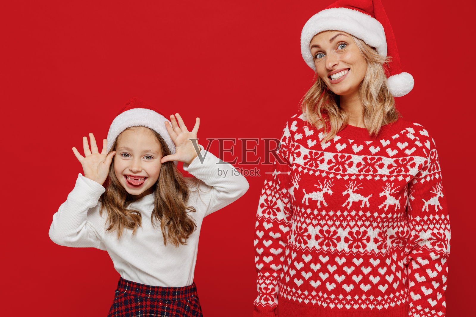 年轻开朗的快乐的女人穿着毛衣和孩子玩得开心宝贝女孩6-7岁妈妈小女孩女儿愚弄开玩笑孤立在纯红色背景工作室。新年爱家观念照片摄影图片