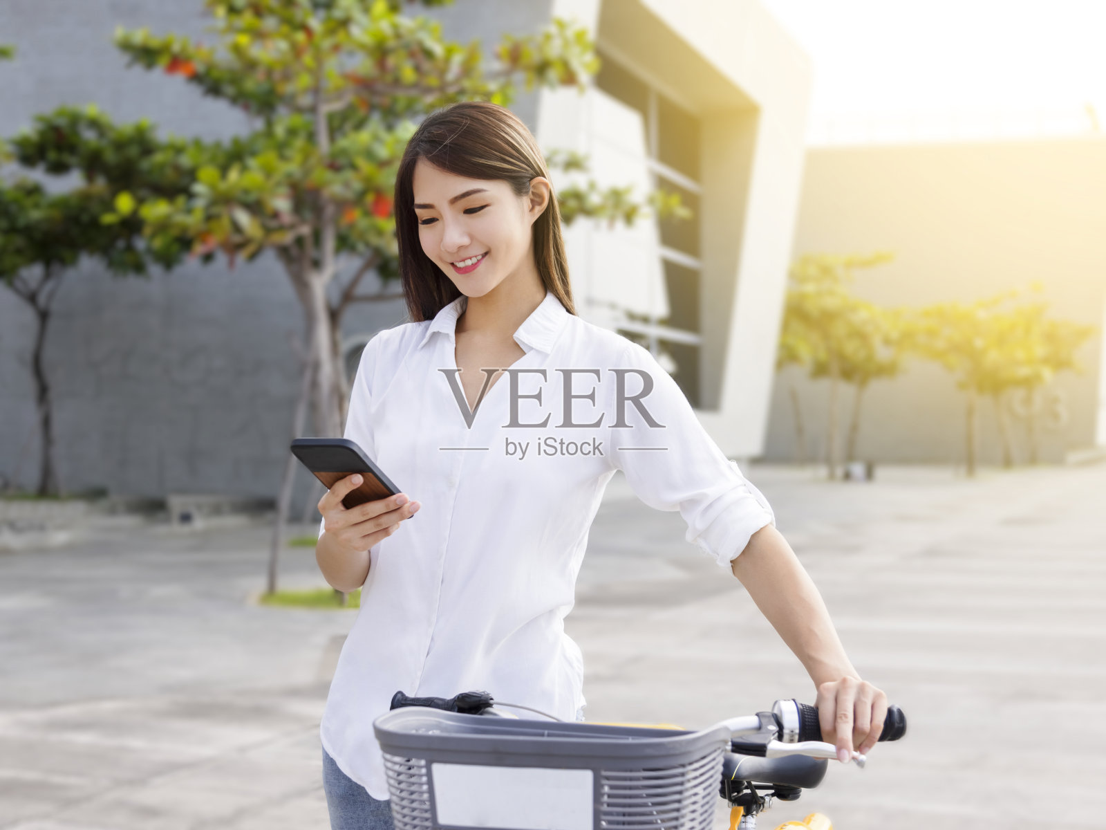 年轻女子在阳光明媚的日子骑自行车时使用智能手机。自行车共享服务。健康的生活方式。“n照片摄影图片