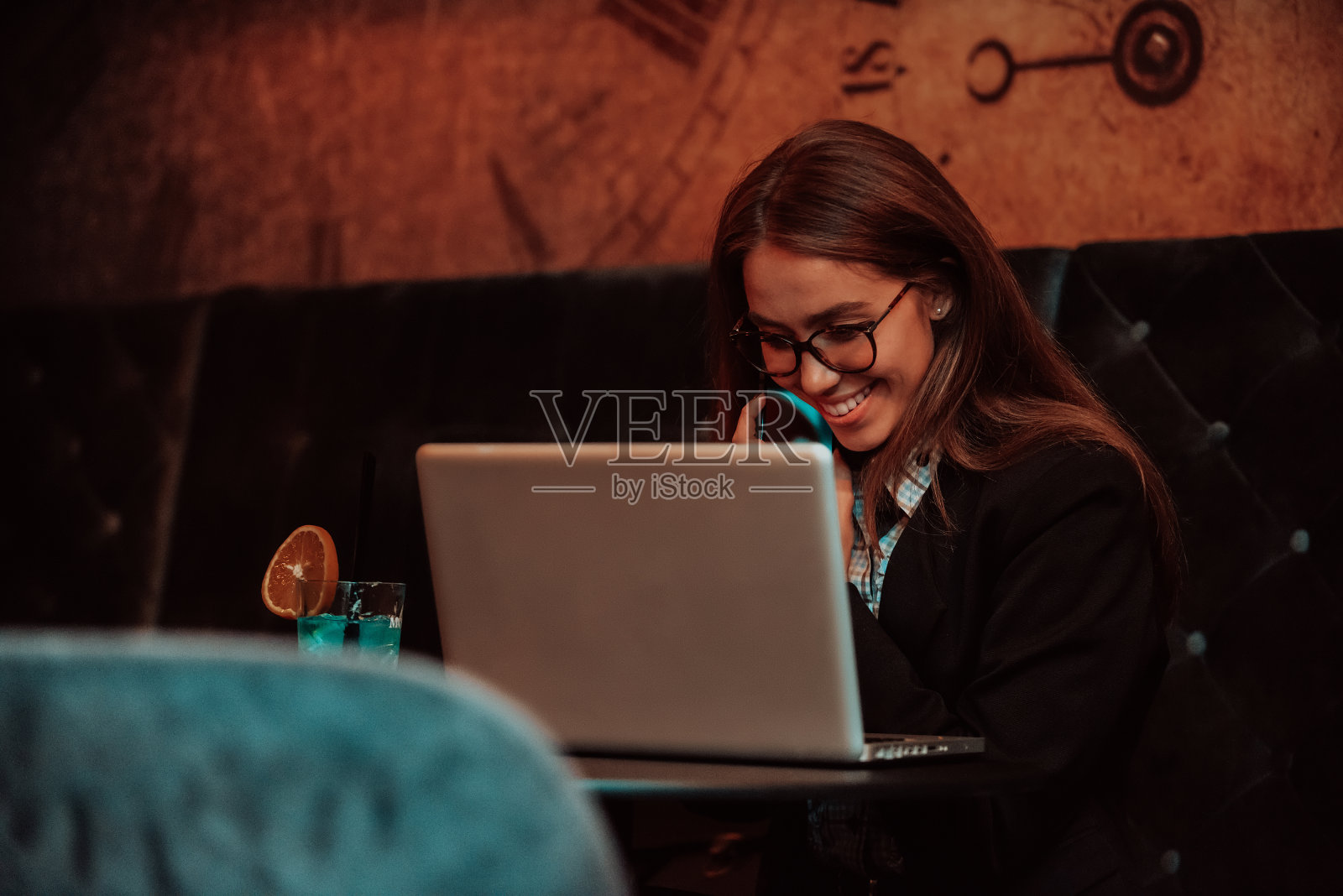 一位戴着眼镜的女商人坐在咖啡馆里，用笔记本电脑和智能手机进行在线会议。有选择性的重点照片摄影图片