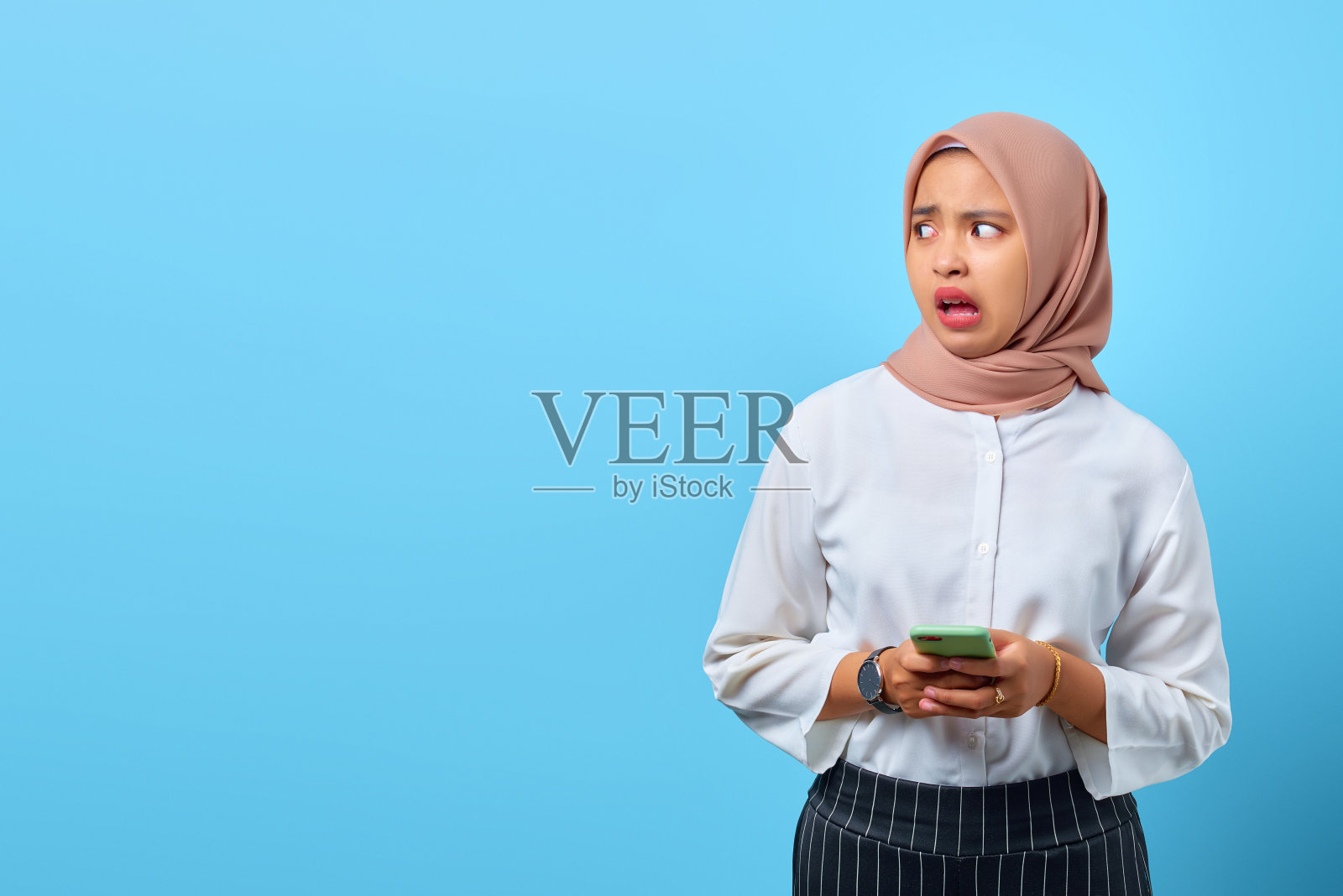 震惊的年轻亚洲女人的肖像，张着嘴看向一边使用手机照片摄影图片