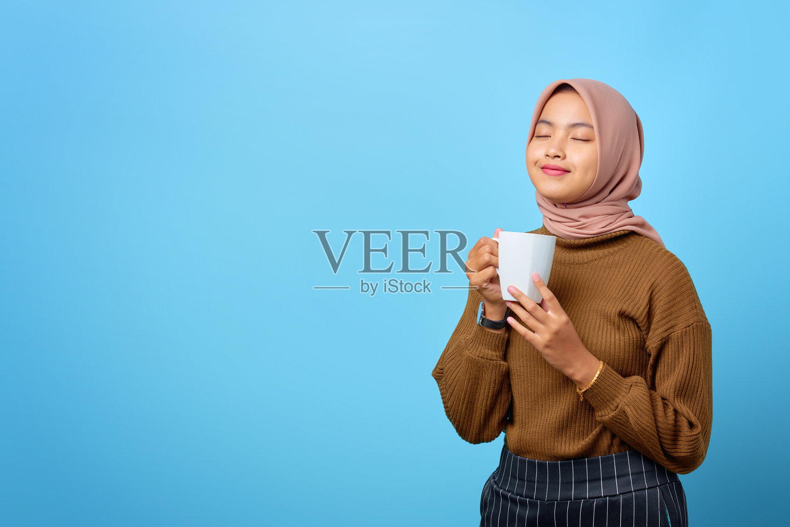 美丽的年轻亚洲女人拿着杯子和喝茶在蓝色的背景照片摄影图片