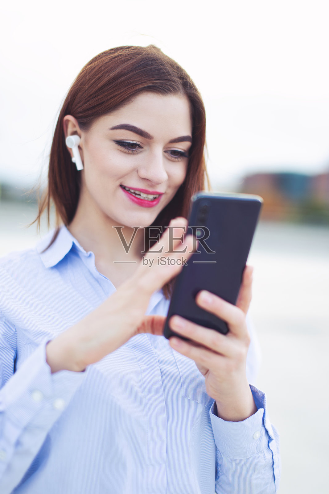 快乐的年轻红发女商人带着免提设备和智能手机在户外照片摄影图片