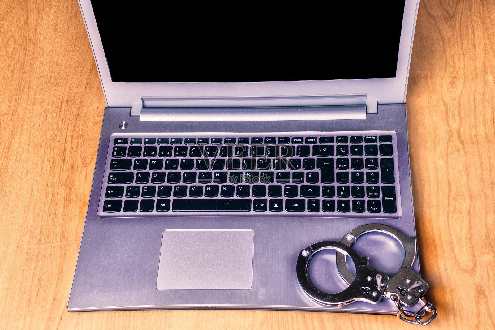 桌上放着银色笔记本电脑和银色手铐。网络安全的概念。照片摄影图片