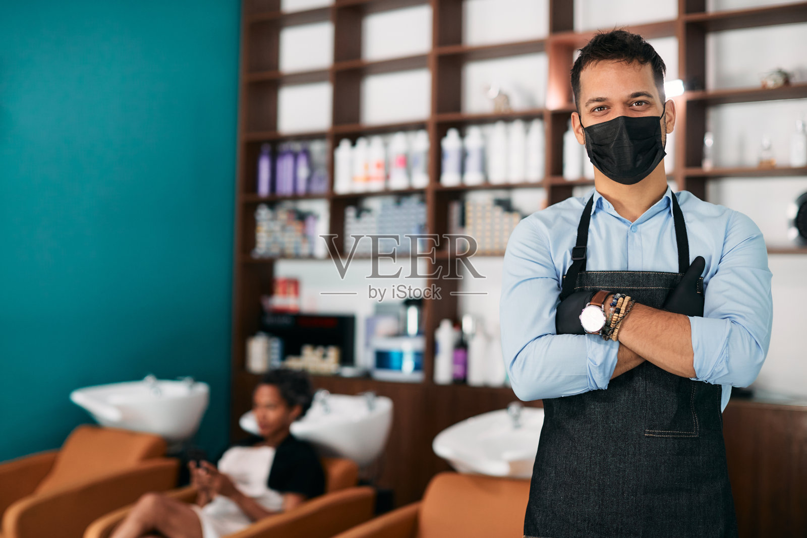 自信的美发师在美发沙龙戴着防护口罩看着镜头。照片摄影图片