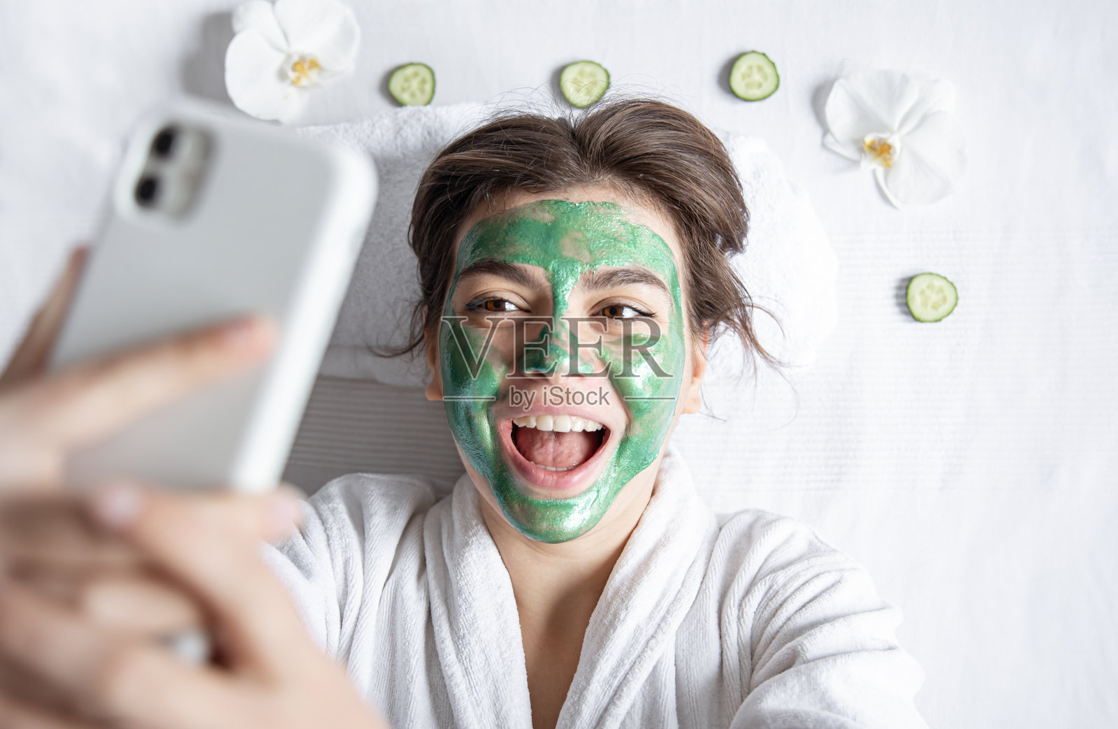 一名年轻女子戴着化妆面具，用智能手机自拍。照片摄影图片