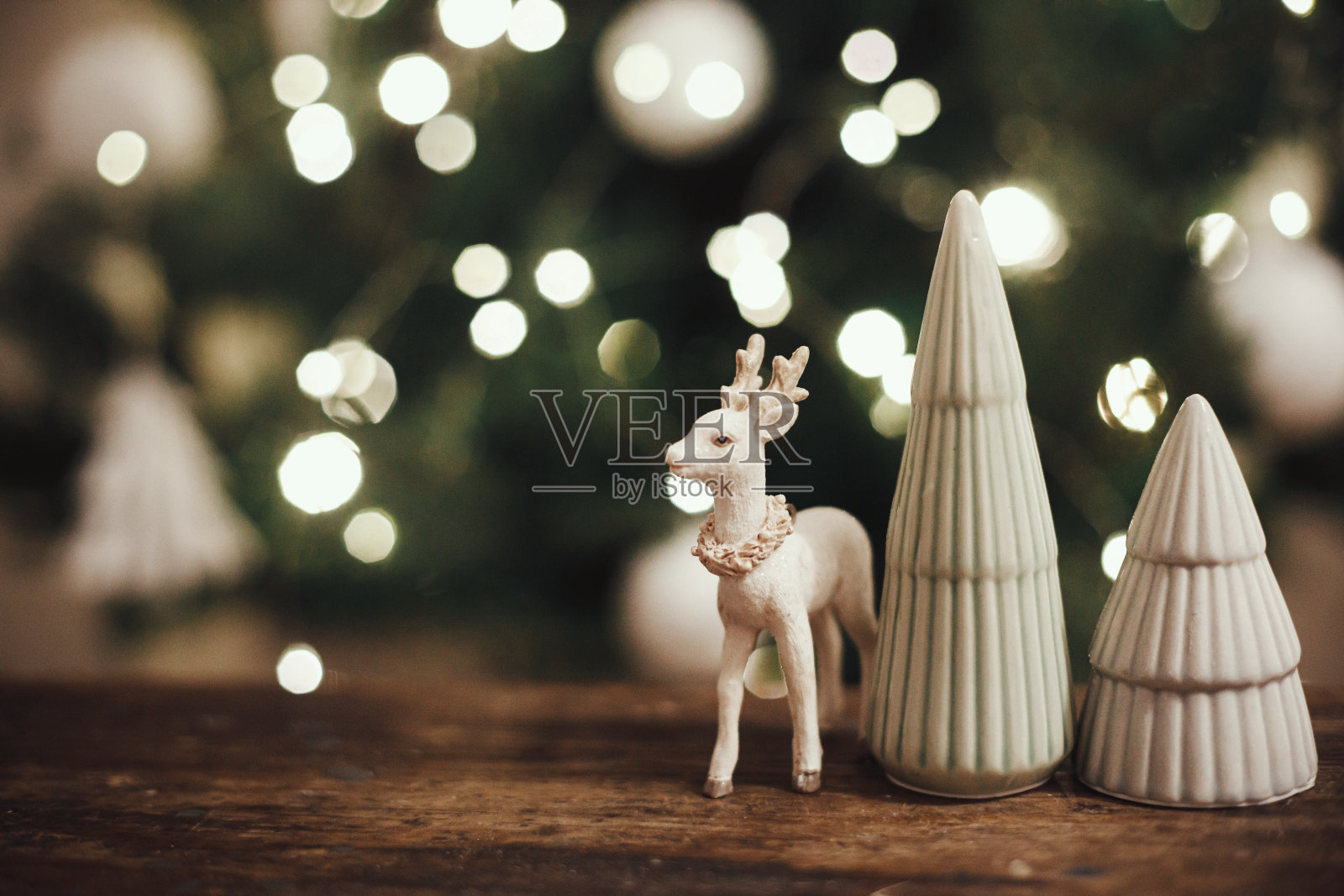 时髦的驯鹿玩具和圣诞树上质朴的木头背景上的圣诞灯。美丽的小圣诞场景在喜庆的斯堪的纳维亚房间。空间的文本。圣诞快乐照片摄影图片