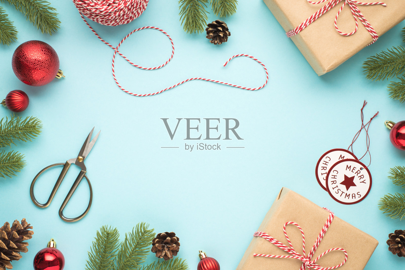 顶部视图照片的松枝圆锥红色的圣诞树球剪刀卷轴装饰绳快乐的圣诞节标签和两个手工纸礼品盒在孤立的淡蓝色背景与空白照片摄影图片