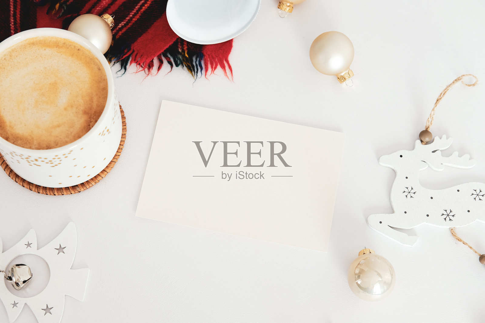 北欧风格的圣诞作文。平铺空白贺卡模型，肉桂棒，咖啡杯，铃，球，针织帽子，木制圣诞装饰在白色的桌子上。Hygge，舒适的家居装饰c照片摄影图片