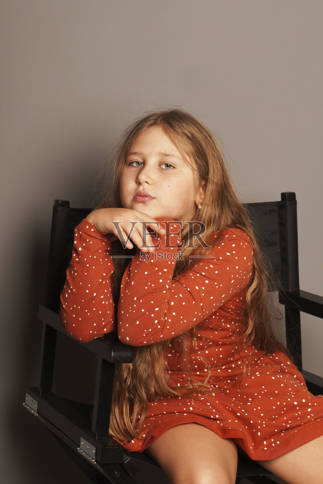 年轻快乐滑稽微笑长发女孩坐在黑色扶手椅上的灰色背景。照片摄影图片