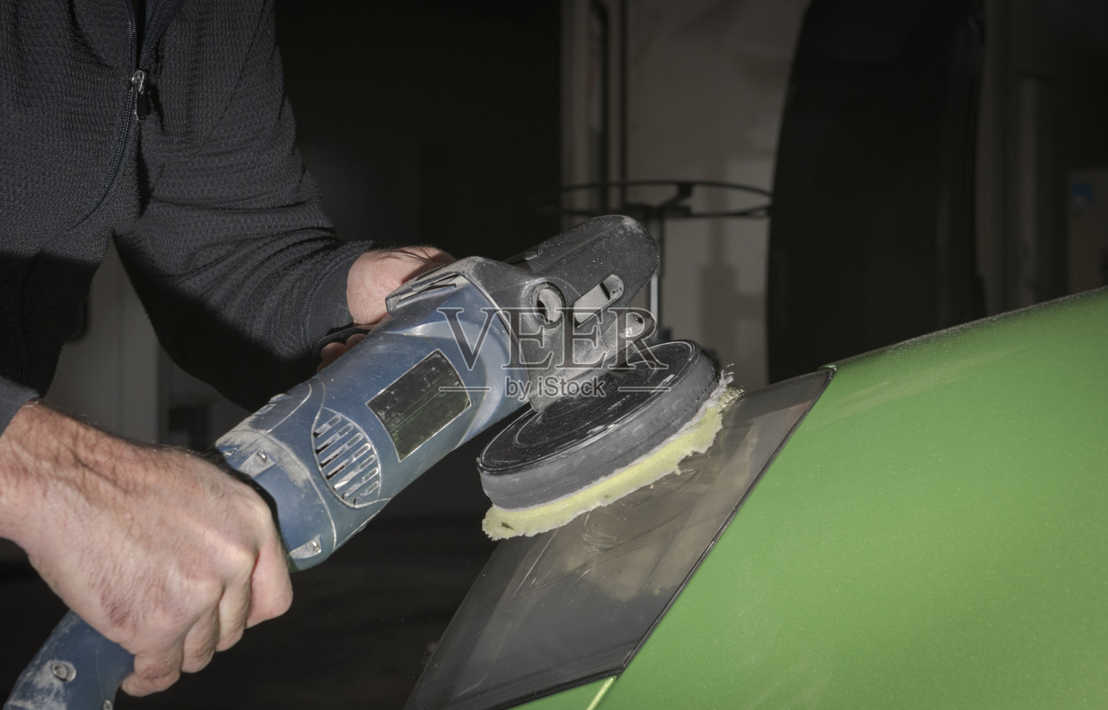 抛光汽车大灯。汽车维修工用电动抛光机抛光绿色汽车引擎盖照片摄影图片