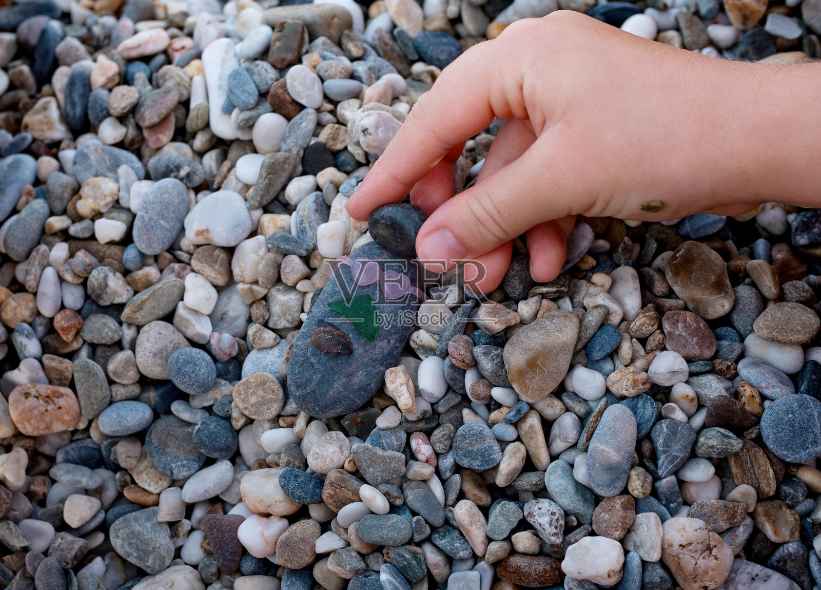 夏日的卵石沙滩上，孩子们戴着太阳镜，正在制作卵石石。照片摄影图片