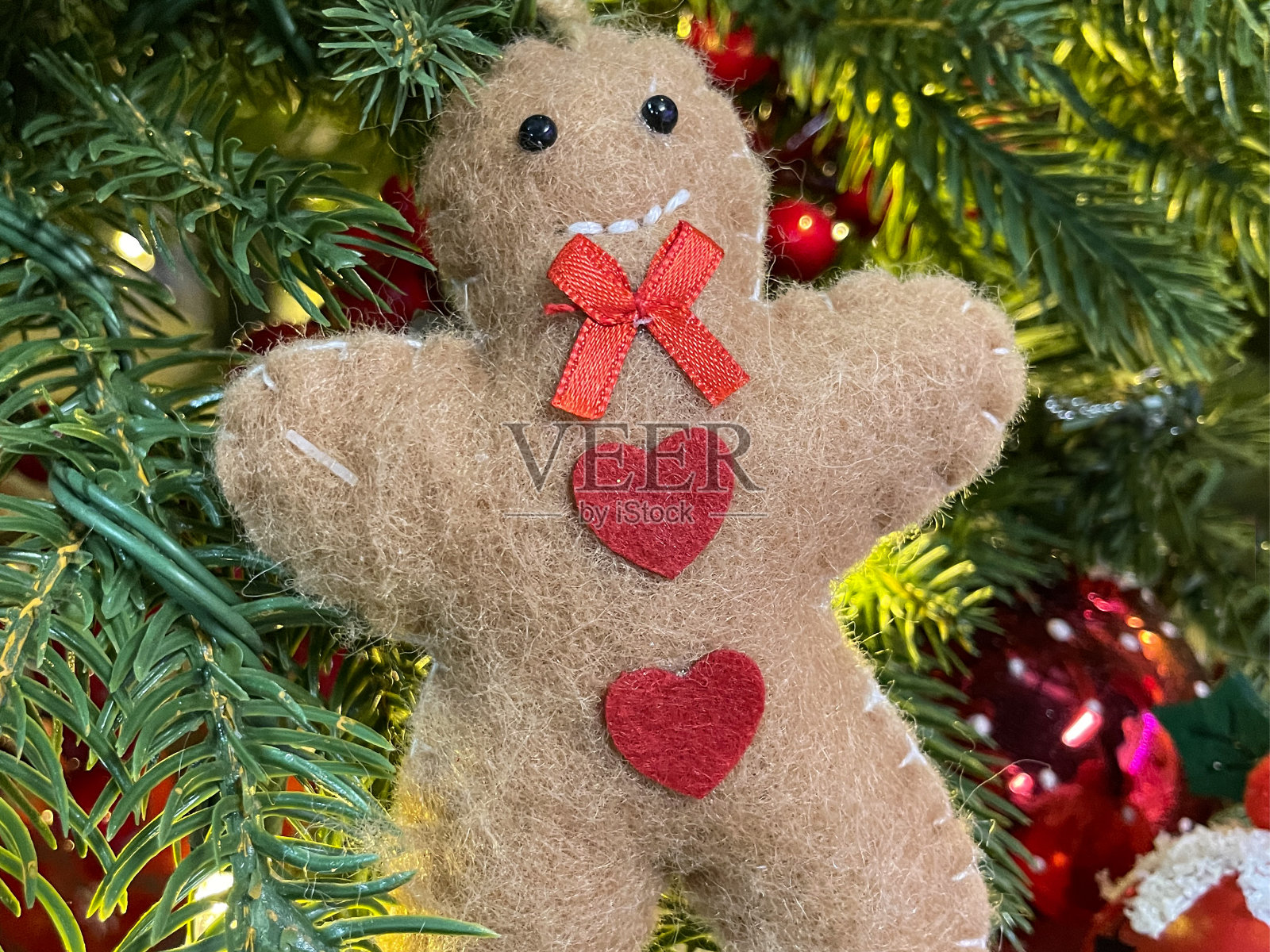 特写图像的感觉姜饼人装饰红色领结和心形装饰，在人造圣诞树树枝，云杉针，模糊的白色精灵灯的背景照片摄影图片