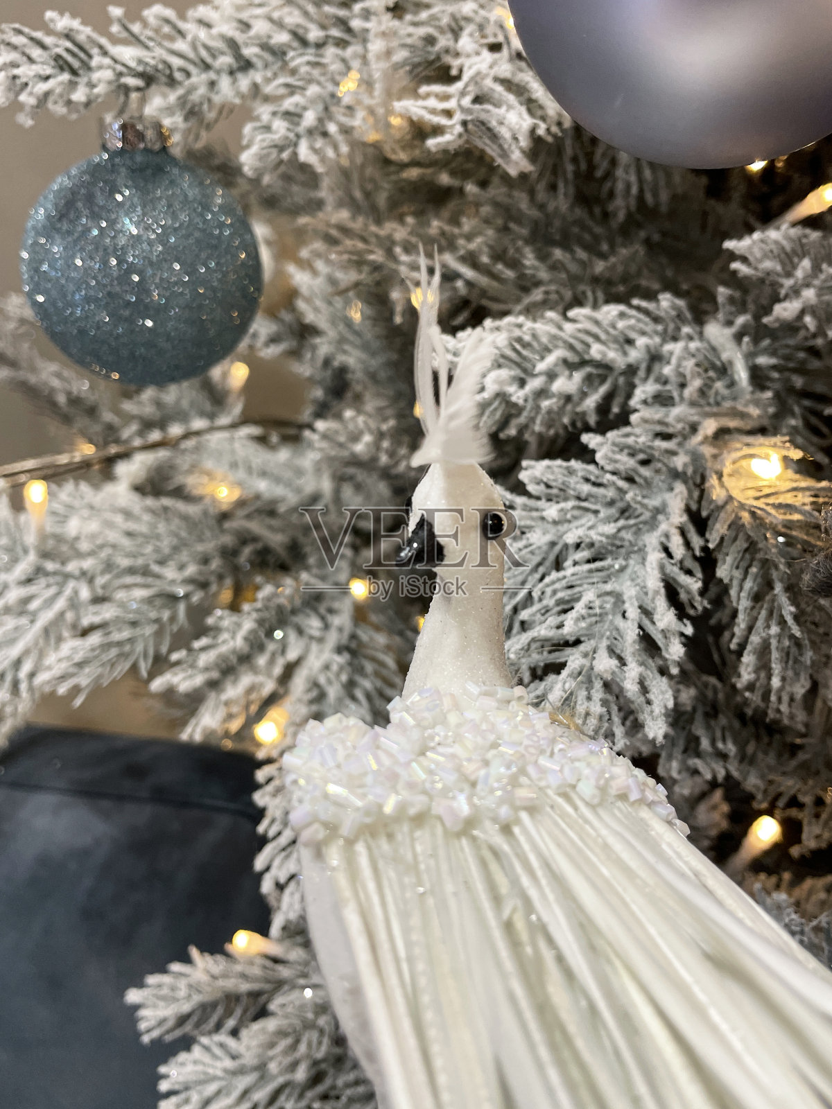 图像中的白鸽装饰，银色和蓝色的闪光小饰物挂在人造圣诞树的树枝上，云杉针覆盖着人造喷雾雪，模糊的白色精灵灯的背景照片摄影图片