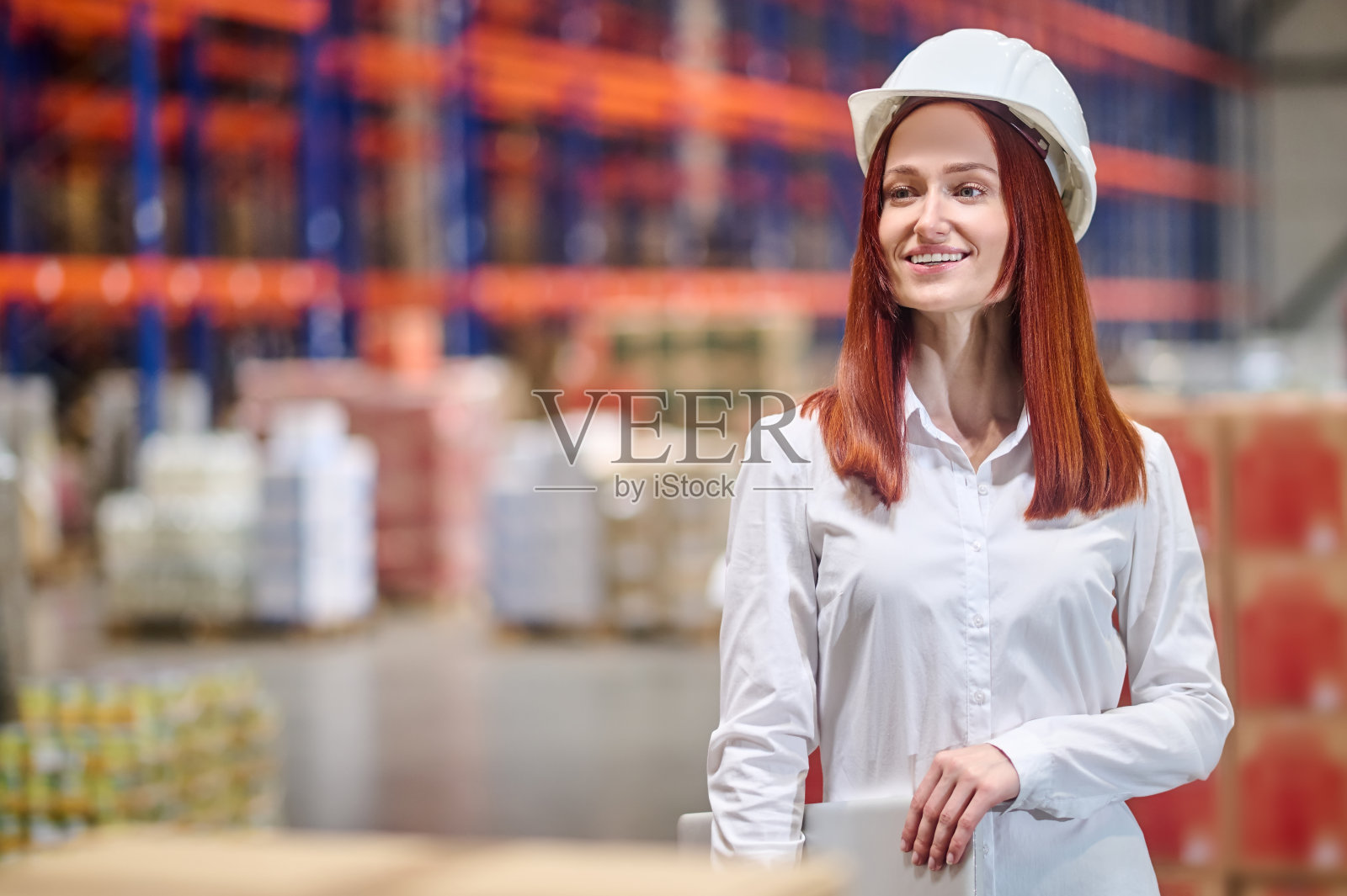 一个坚定的女人戴着头盔，手提电脑在仓库里照片摄影图片