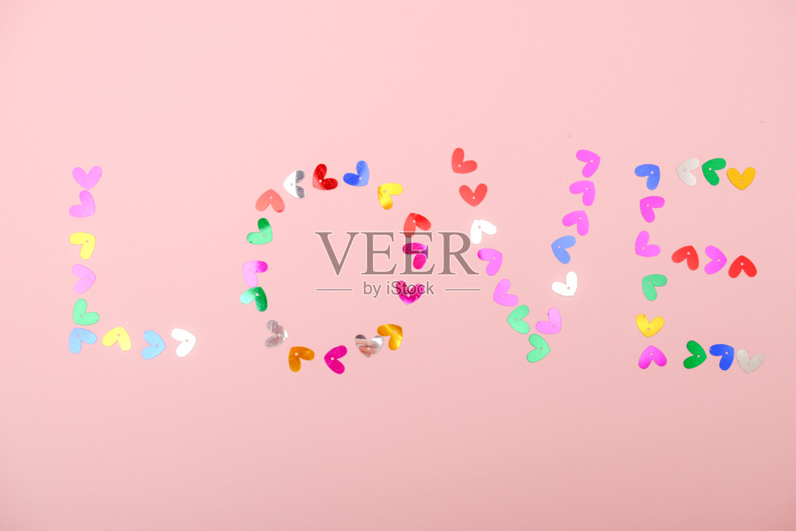 “爱”字由心形的五彩纸屑做成，放在粉红色的背景上照片摄影图片