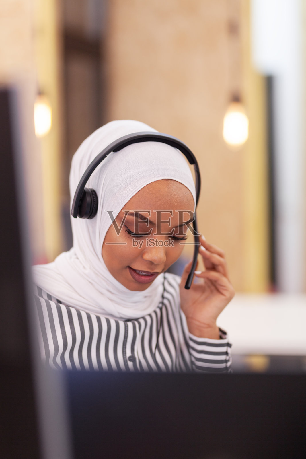 戴着头巾和耳机的非裔美国穆斯林女孩在现代办公室中。客户服务呼叫中心照片摄影图片