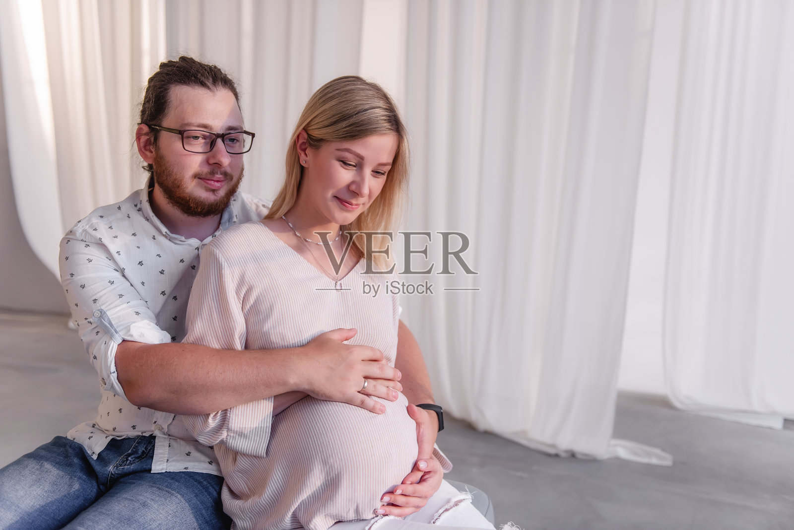 家庭的近距离肖像期待着孩子。长胡子的男人抱着孕妇的肚子照片摄影图片