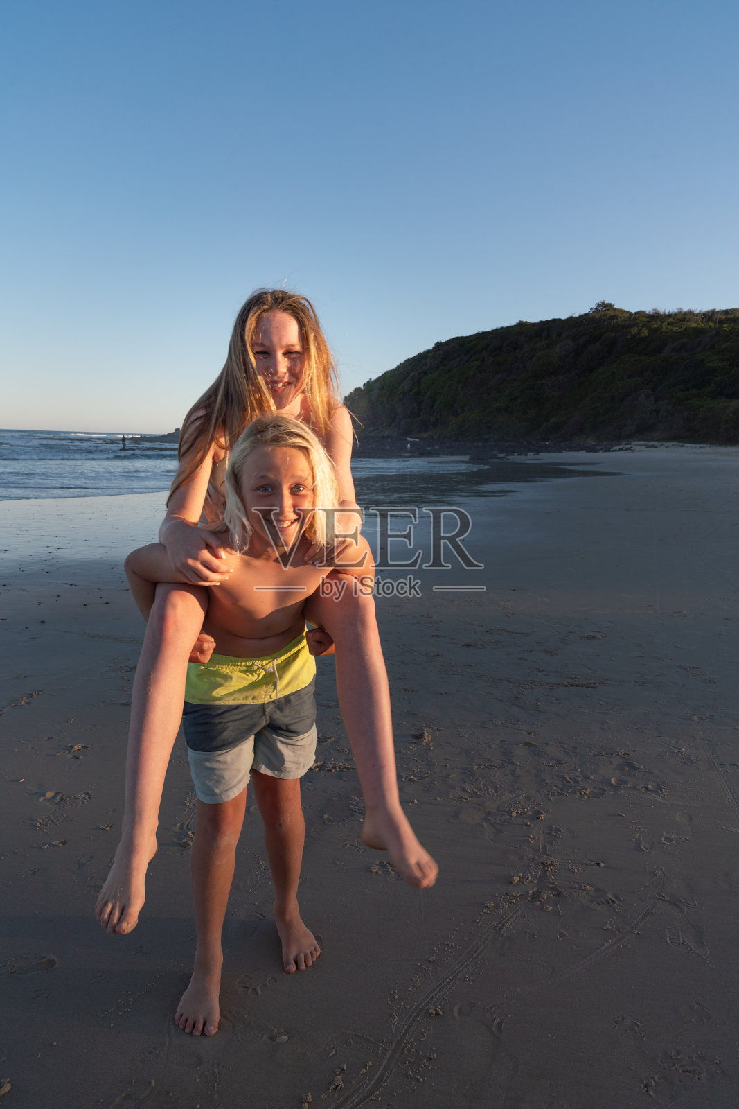 在午后的阳光下，一个男孩背着一个女孩在海滩上照片摄影图片