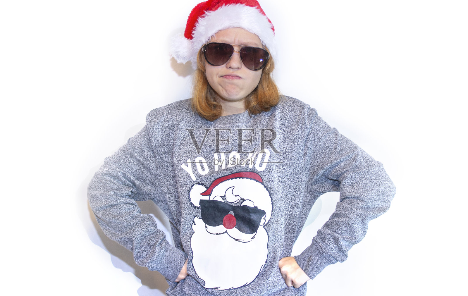 一个红头发的女孩生气地看着镜头。红头发的学生看到圣诞礼物打折很生气。满脸雀斑的女学生穿着圣诞老人的毛衣照片摄影图片