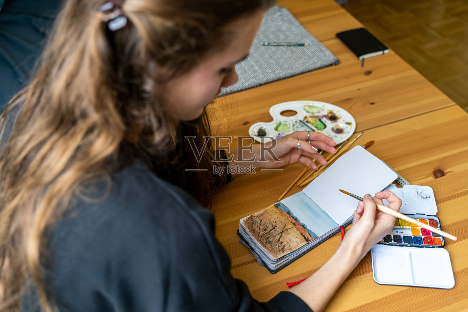 深色皮肤的女人用水彩在纸笔记本上画自然风景照片摄影图片