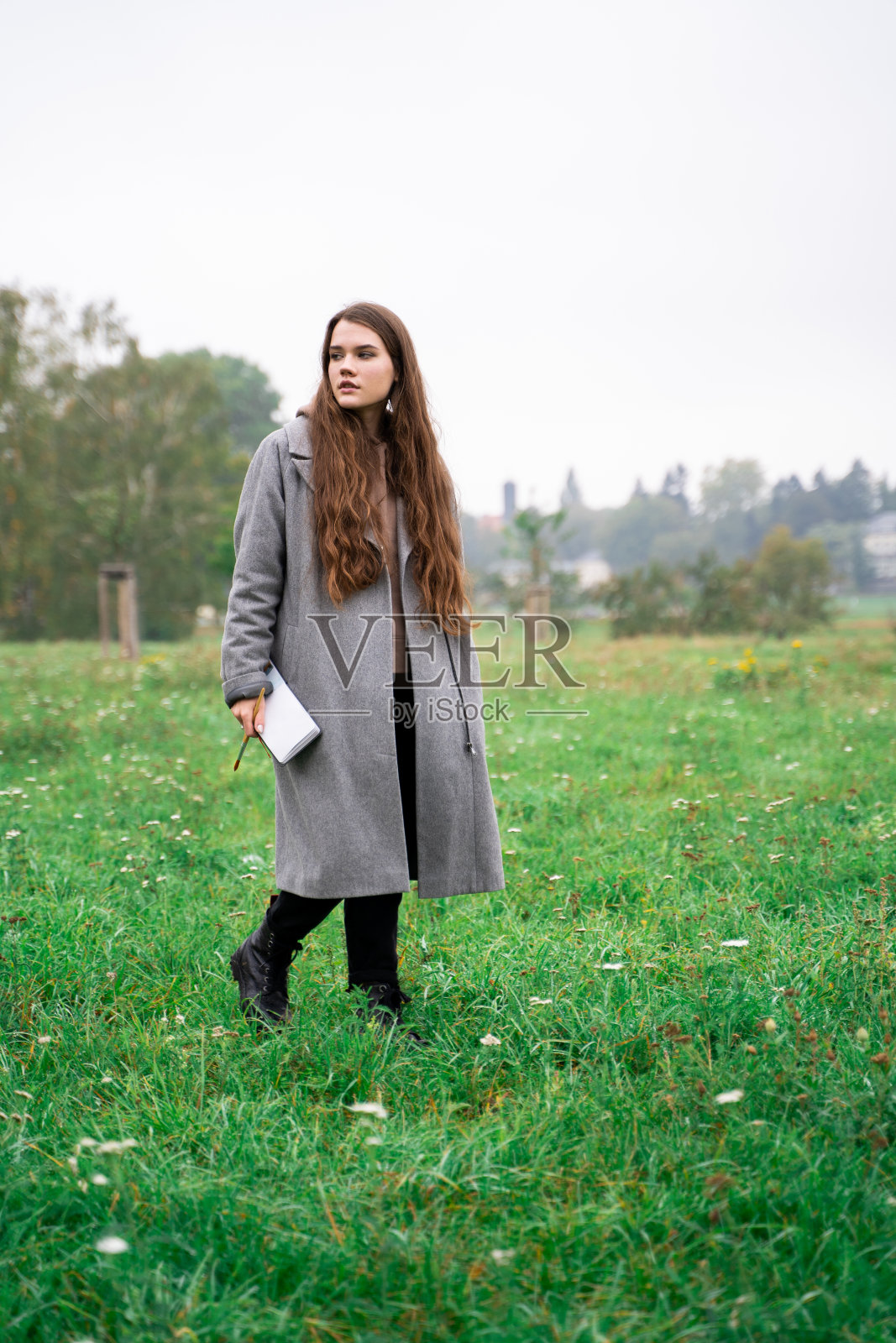 年轻的黑发女人穿着外套在绿色清新的公园在白天散步照片摄影图片