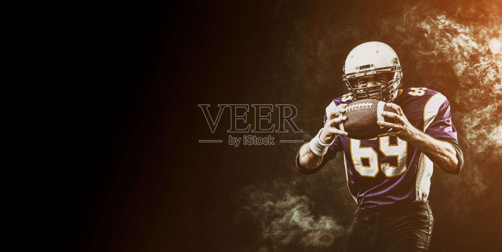 美国橄榄球运动员，手里拿着冒烟的球。黑色背景，复制空间。美式足球的概念，动力，复制空间照片摄影图片