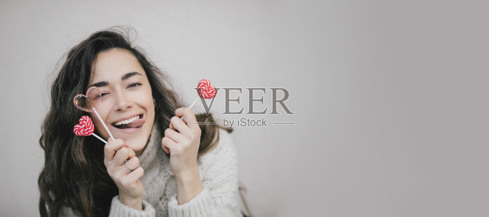 年轻美丽的女子在白色背景下与情人节心形糖果和棒棒糖合影。照片摄影图片