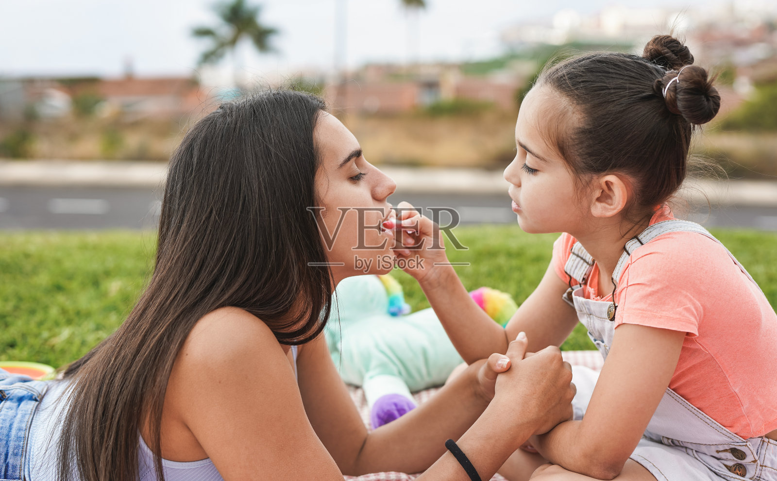 西班牙可爱的小女孩在花园草地上用口红给她的姐姐化妆照片摄影图片