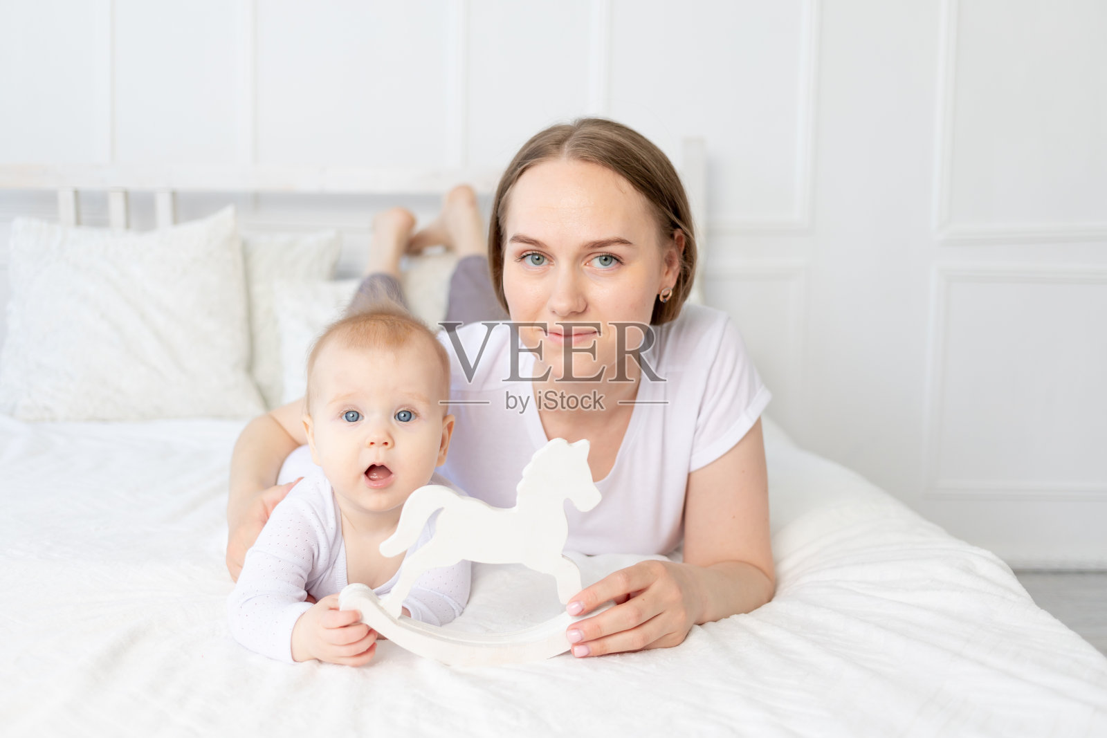 妈妈在家里的床上和宝宝玩木制玩具马，一家人快乐照片摄影图片