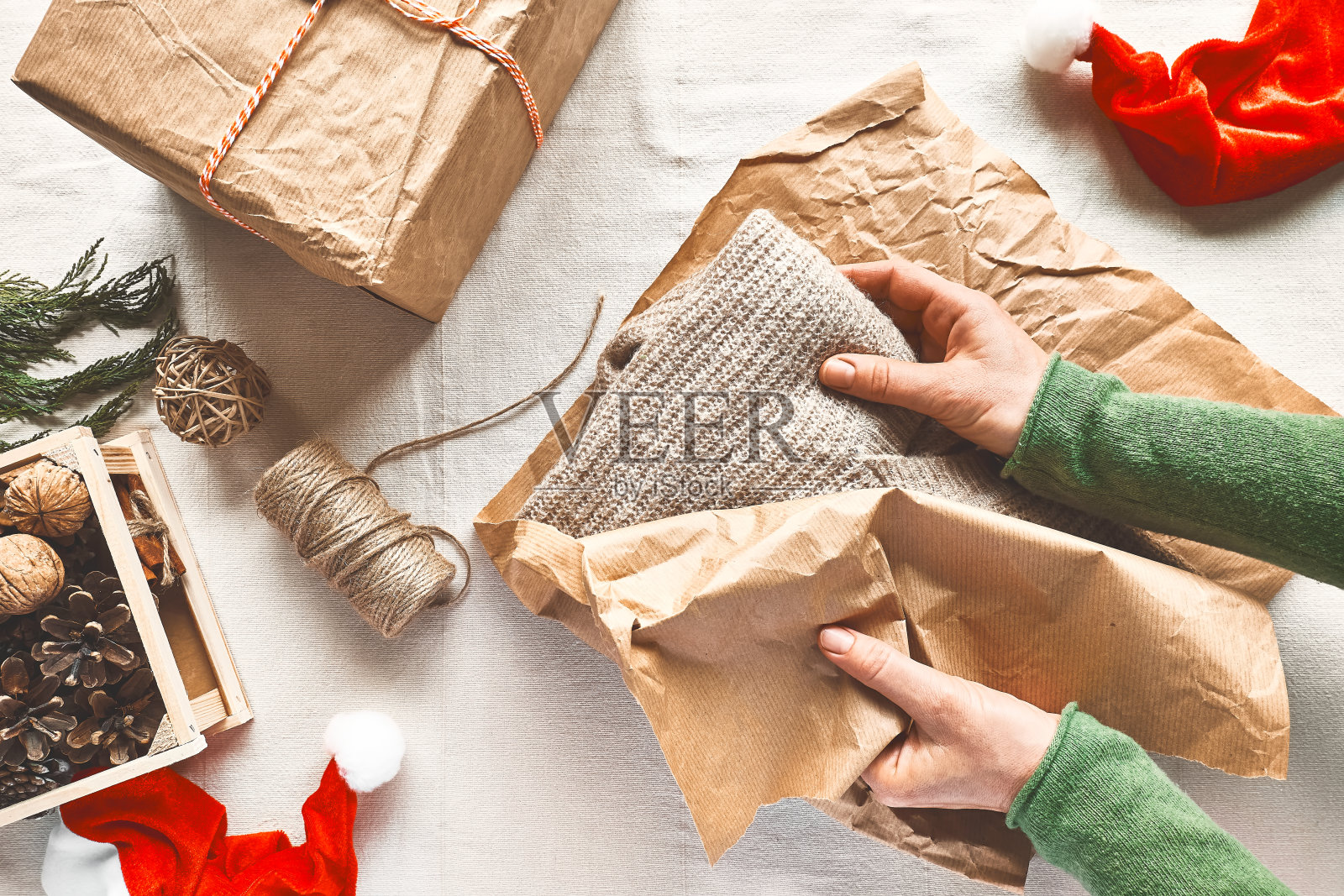 在圣诞装饰的桌子上，女人的手用工艺回收纸包裹羊毛衫。自然审美。“零浪费”。圣诞礼物的包装。冬天的节日庆祝活动。前视图。照片摄影图片