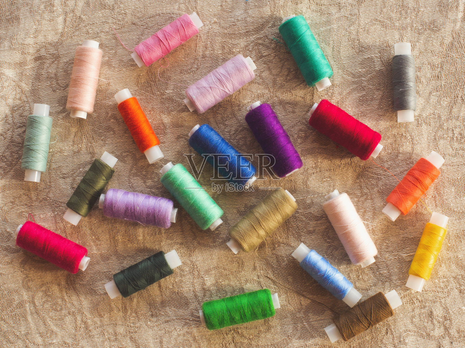 颜色鲜艳的橙色、黄色、红色、蓝色、绿色的线轴，在棕色的乡村亚麻织物上。图案背景用于缝制或手工制作店铺网站或社交网络页面设计或广告照片摄影图片
