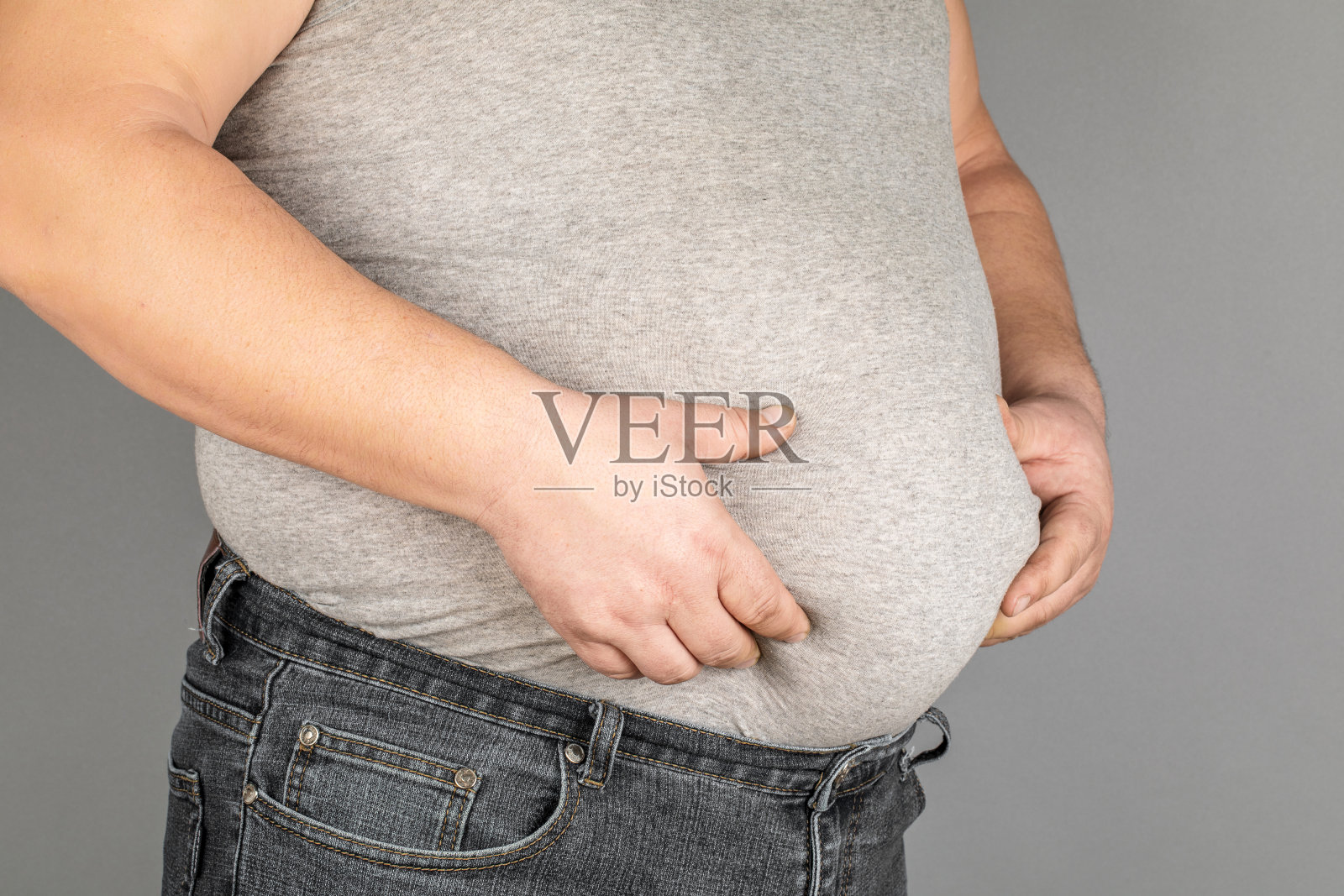 一个胖子，在灰色的背景上检查他的体重。照片摄影图片