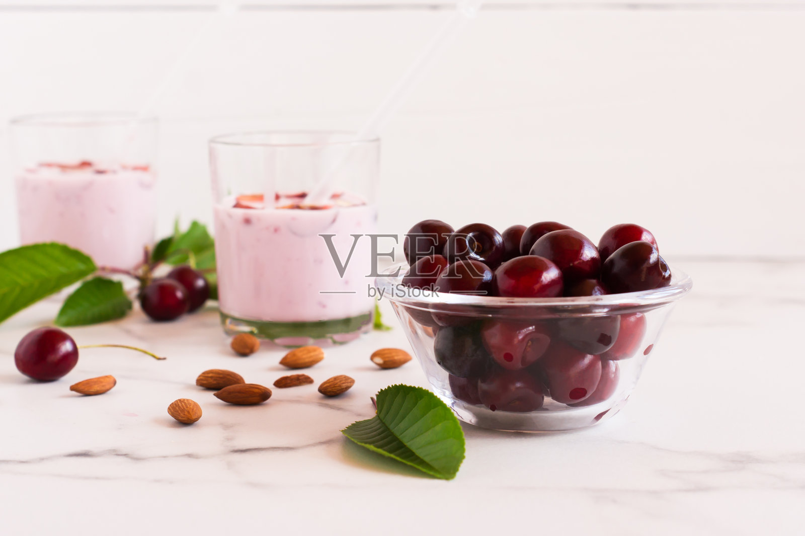 碗里放着成熟的樱桃，大理石白色的桌子上放着两个玻璃杯和樱桃冰沙。有机健康食品。照片摄影图片